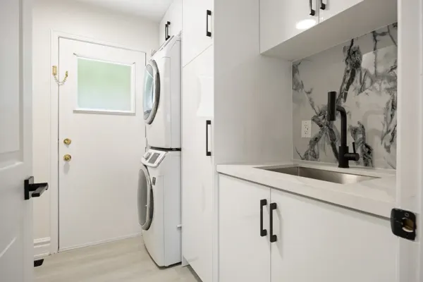 Completed laundry cabinetry, stacked appliances and sink